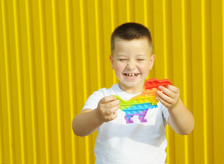 Smiling boy holding a toy pop it on a yellow background
