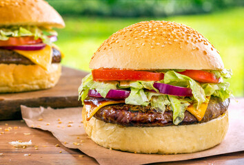 Two delicious Hamburgers on a wood desk with green grass nature background