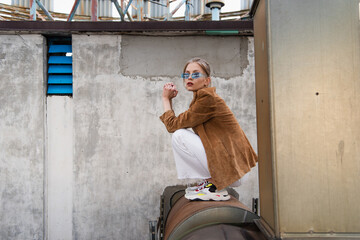 full length of young woman in trendy outfit and blue sunglasses posing on rusty construction
