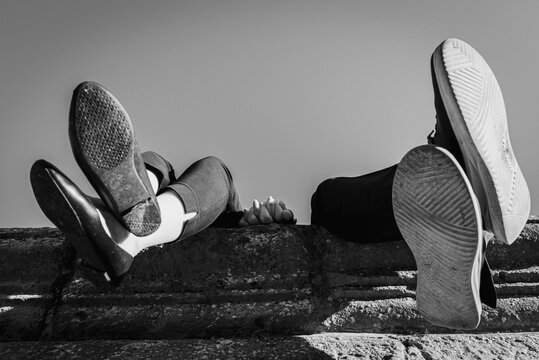 Black and white photo, bottom view. couple sitting on old wall, dangling legs, close up view. Their faces are not shown.