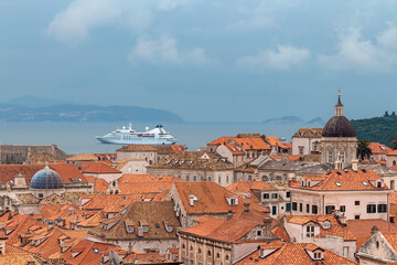 Fototapeta premium top view of the red tiled roofs of the ancient Croatian city of Dubrovnik and a white cruise ship on the sea