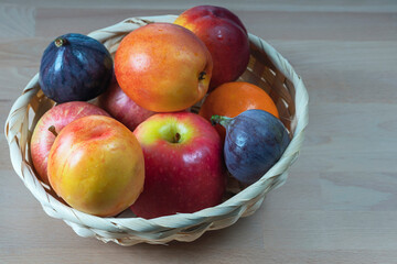 ripe delicious apricots, apples and figs in a wicker basket on a wooden background