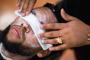aplicando crema limpiadora en peluqueria latina para proceder al corte de pelo. anillos y reloj en las manos del barbero.peluquero .