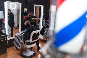 barber cutting the hair of a young man. in a barber shop for all ages and styles. seen from behind the glass..