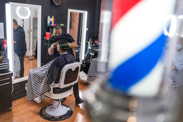 barber cutting the hair of a young man. in a barber shop for all ages and styles. seen from behind the glass..