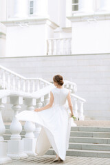 portrait of the bride with flowers in a beautiful wedding dress in full growth climbing the stairs, a young blonde, gentle photo wedding portrait