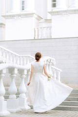 portrait of the bride with flowers in a beautiful wedding dress in full growth climbing the stairs, a young blonde, gentle photo wedding portrait