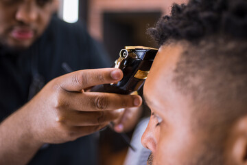 hairdresser cutting young man's hair in latin barber shop with hair clipper carefully. .