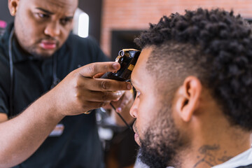 hairdresser cutting young man's hair in latin barber shop with hair clipper carefully. .