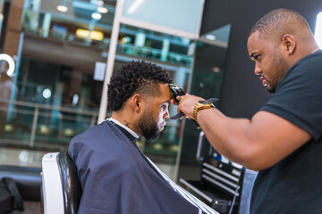 hairdresser cutting young man's hair in latin barber shop.with hair clipper carefully in front of mirror.