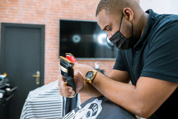 barber holding hair clippers.red and black hair clippers in barber's chair years. chairs covered by barber's blanket.