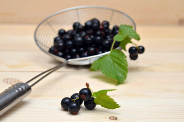 a bunch of black currants with leaves on a wooden background and berries in a colander