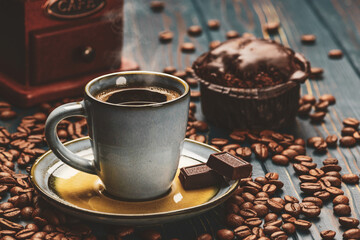 Cup of coffee on a blue wooden table with coffee beans and a chocolate