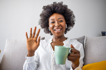 Happy african american young business woman wearing wireless headphones, looking at computer screen, waving hello. Pleasant attractive mixed race female professional holding video call with client.