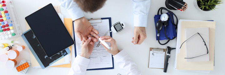 Doctor taking blood test from patients finger with lancet top view
