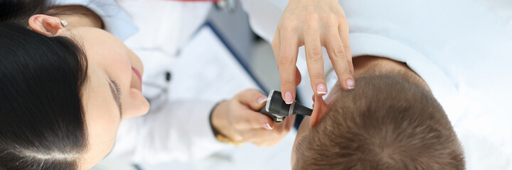 Otorhinolaryngologist examining patient with otoscope top view closeup