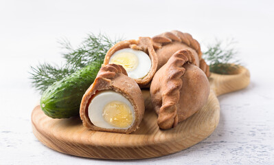 Russian traditional rye pies with egg, kokurki, on light gray background with cucumber and herbs. Delicious homemade food and snack © olepeshkina