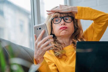 stressed out woman looking at cell phone at home with computer - obrazy, fototapety, plakaty
