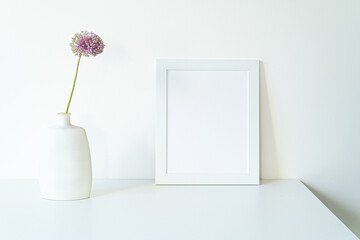 Empty white picture frame mockup. Modern and elegant vase with allium ampeloprasum flower over...
