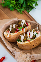 Authentic fresh falafel balls inside of two halves of pita bread sandwich with chopped salad, red hot peppers, lemon, a drizzle of tahini sauce. chickpea falafel in a fluffy pita on a wooden board