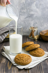 Milk is poured into a glass next to oatmeal cookies on a wooden table 