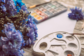 Palette of watercolor paints, brushes and paper for a water color on wooden background, close up. Flat lay, spring background with copy space