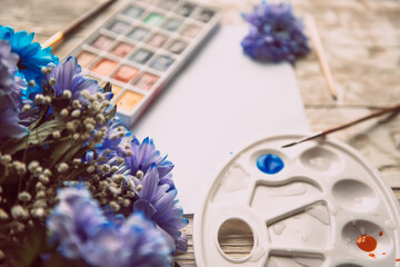 Palette of watercolor paints, brushes and paper for a water color on wooden background, close up. Flat lay, spring background with copy space
