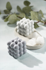 Two grey-blue bubble candles on a concrete tray and white crystals on pastel blue background