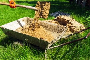 Fototapeta premium A master builder pours sand into a cart with a shovel to make concrete. Close-up of a foreman's hand during construction work