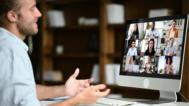 Group brainstorm, online business briefing. Successful caucasian man uses computer for a video call, virtual meeting with partners, sits at workplace, diverse multiracial people on the computer screen
