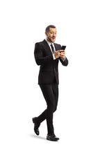 Full length portrait of a smiling businessman walking and using a mobile phone