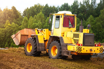 Obraz premium A yellow bulldozer is compacting a green mass of cut grass. 
