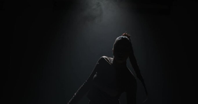 Cool girl dancing ethnic passionate dance or hip-hop in spotlight in dark studio. Female dancer show rhythmic moves