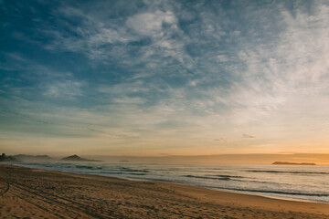 Fototapeta na wymiar A lush dawn on a Brazilian beach called Gamboa with blue sky, clouds and islands with the sun rising in the background in Garopaba - SC