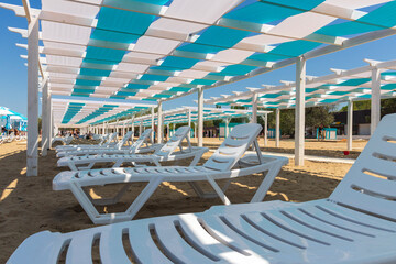 Anapa. Krasnodar Territory - May 14, 2021: canopies, gazebos painted in blue and white stripes, architectural structures made of wood and white sun beds on the Black Sea beach