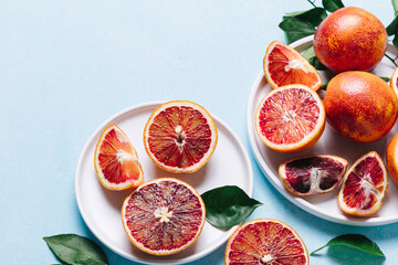 Composition of whole and sliced blood oranges in a plate on light blue table background. Flat lay,...