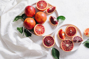 Composition of whole and sliced blood oranges in a plate on white table background. Flat lay, top view.