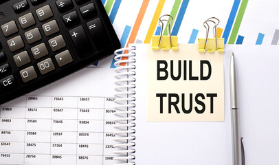 BUILD TRUST text, written on a sticker with calculator,pen on chart background.