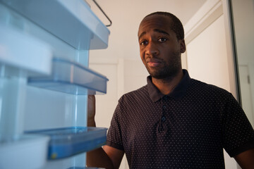 An African American boy opens the fridge and realizes it is empty. He has a sad and worried facial...