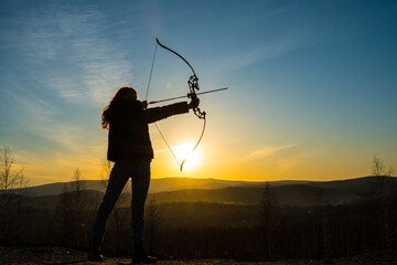 Girl with bow, shooter hunter on the background of the sunset.
