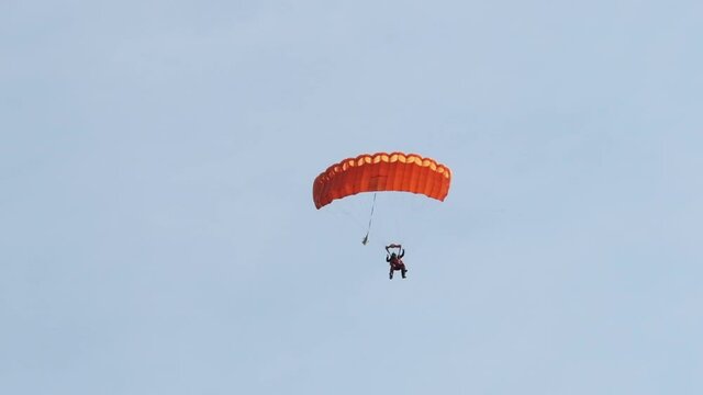 Parachutists in tandem flying in the sky with a parachute. Slow Motion. Tandem jump. View from ground. Skydiver flying with parachute against the sky. Extreme sport. Two people flying.