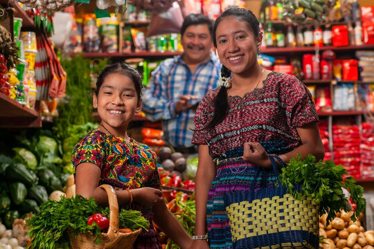 Happy indigenous girls looking at the camera in a grocery store and a salesman behind them.