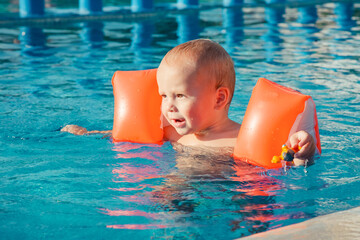 Cute little baby boy playing in outdoor swimming pool on hot summer day. Kids learn to swim. Happy...