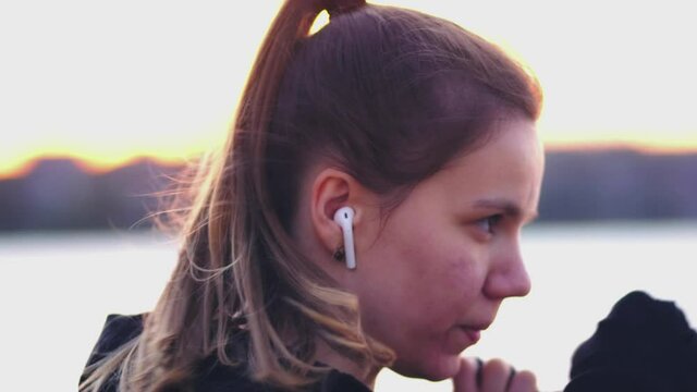 Slow motion. A young female boxer punches the air in black armbands and headphones on the beach at sunset. Shadow fight. Outdoor sports. Close up