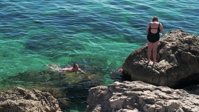 Tourists swim in the open Black Sea among the rocks on a clear sunny summer day.