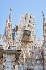 View from the bottom of Duomo cathedral building during reconstruction process with multiple metal scaffolding mounted to facade, building facade renovation. Milan, Italy