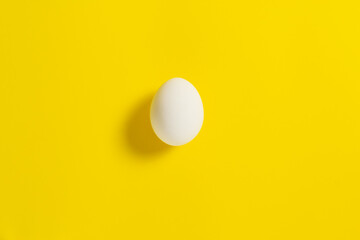 One white chicken egg lies on a yellow background.