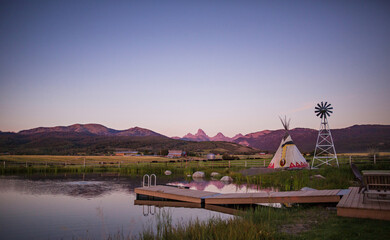 A lake with a dock, a teepee and a windmill with the Tetons in the background on a ranch in Alta, Wyoming, on the west side of the Teton Mountains.  © julie