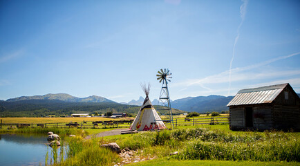 A lake, a teepee and a windmill with the Tetons in the background on a ranch in Alta, Wyoming, on the west side of the Teton Mountains.