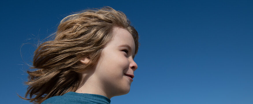 Portrait Of A Small Blond Boy Looking Away On Blue Sky With Copy Space, Closeup Banner. Cute Kids Face. Positive Emotional Child.